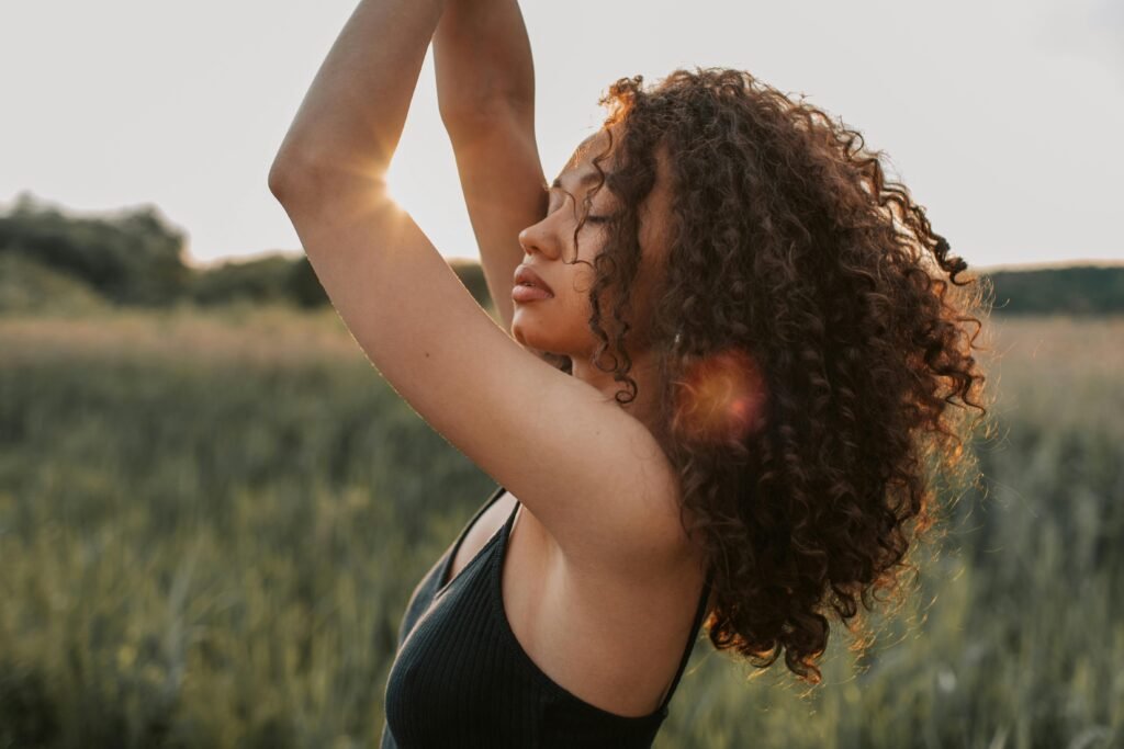 pexels-photo-4668541-4668541 A fashionable woman with curly hair poses confidently outdoors during sunset.